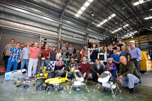 Group of researchers standing behind a variety of robots developed with CSIRO technology.