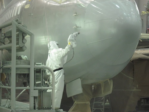 Man spraying topcoat on aircraft nose. 