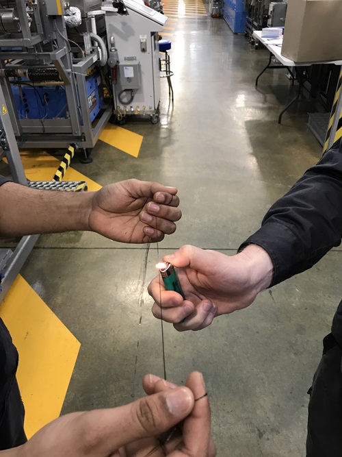 Close up of hands holding a length of carbon fibre while someone places a flame underneath as part of the testing process. 
