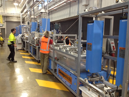 People standing next to the equipment used to manufacture carbon fibre on the factory floor.