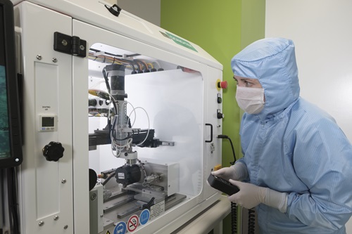 A masked technician works with equipment in a clean room environment.