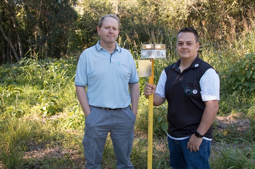 Dr Ash Tews and Dr Philip Valencia standing in vegetation holding the Vertebrate Pest Detect and Deter technology (VPDaD).