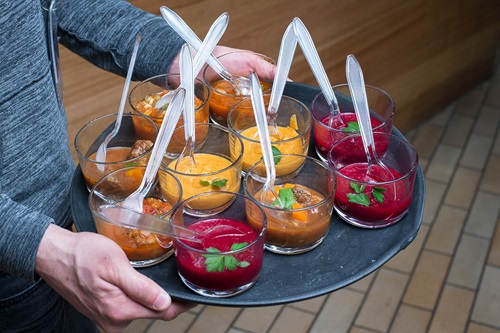 Multiple bowls of coloured food paste with plastic spoons are carried on a circular tray.
