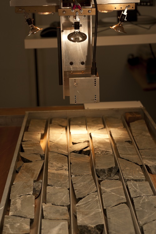 Machine using visible and infrared light to characterise selected minerals from drill cores, chips and pulps on a tray. 