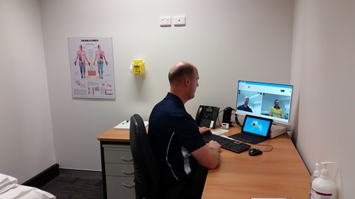 Doctor sitting in front of a computer talking directly with a patient via the Biosymm system.