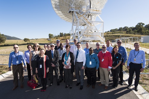 Team members standing in front of radio telescope. 