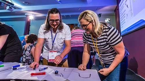 Two primary teacher participants standing at a desk containing STEM related equipment. 