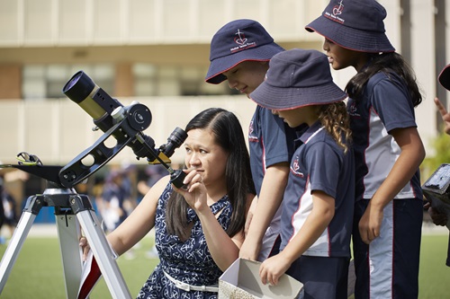 Scientist looking through a telescope with school children looking on.