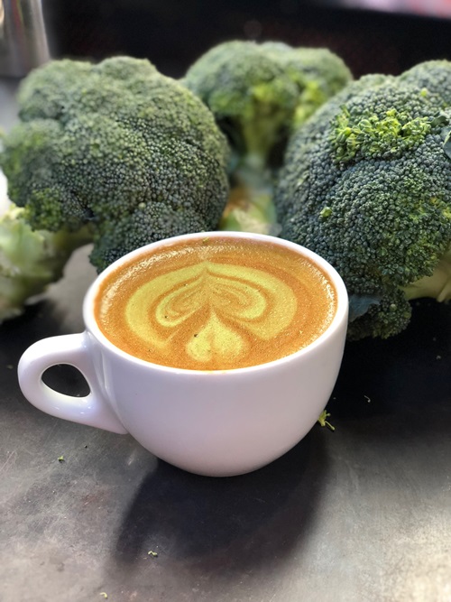 A broccoli latte on a table with broccoli florets in the background.