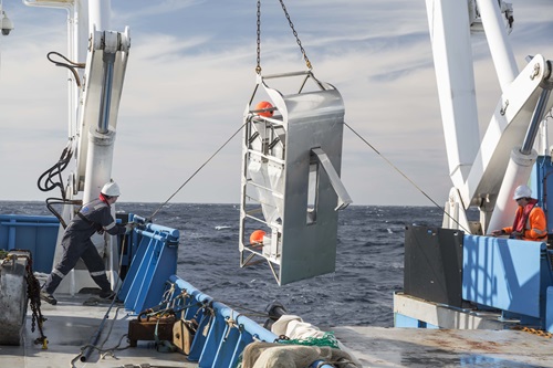 Benthic sled sampling equipment being lower over the side of the ship.