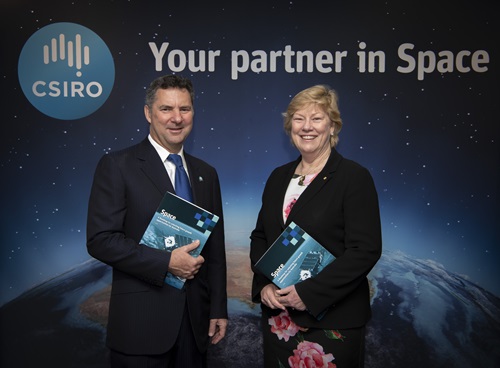 Dr Larry Marshall and Dr Megan Clark standing in front of an earth from space poster holding a copy of the space roadmap. 