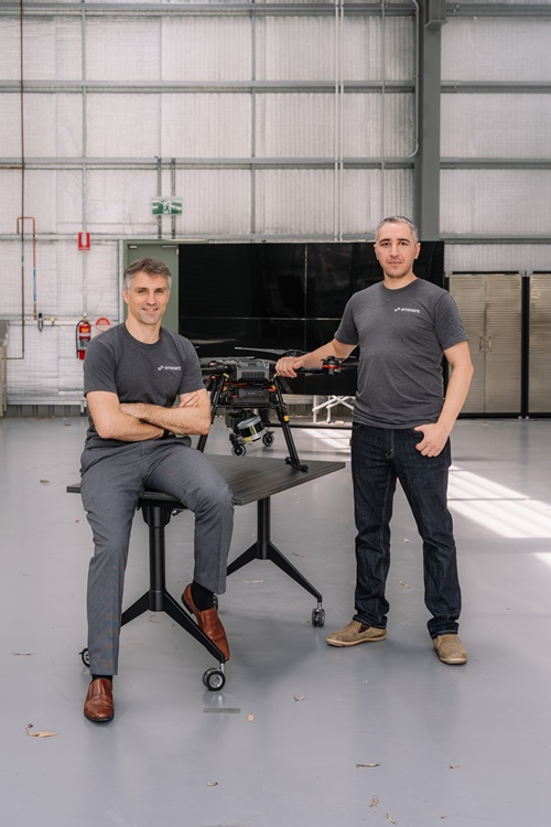 Stefan Hrabar and Farid Kendoul standing next to a chair with a drone resting on it. 