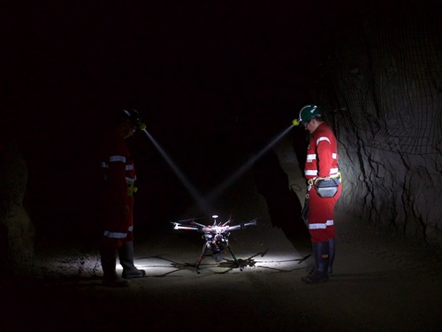 Emesents Hovermap in an underground mine flanked by two people in high-vis clothing wearing hard hats with head lamps.
