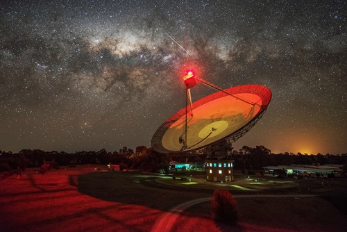 Radio telescope at night illuminated with red light under a starry sky. 