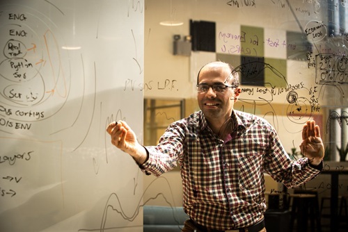 man standing behind glass wall drawing equations on it with black texta