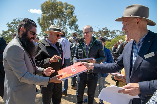 Person handing a park management plan to another person as part of the Victorian parks Joint Management Plan. Other people in the background holding copies of the management plan. 