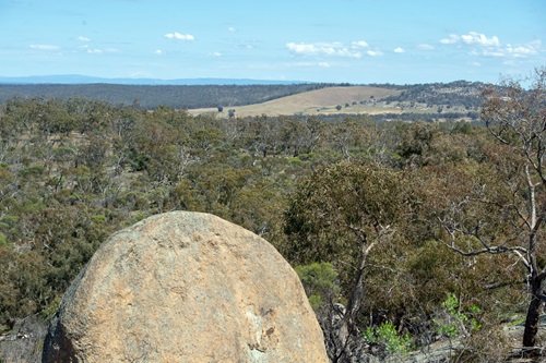Landscape view of Country from the rocky out crops at Melville Caves in Kooyoora State Park, with a large boulder in the foreground, and the view extending across bushland covered hills in the background. 