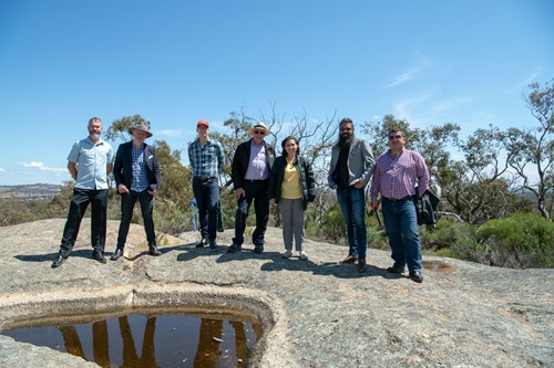Group of people standing around a rock pool located on a rock outcrop with bushland in the background.