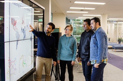 Scientists stand beside an image showing disease movements.