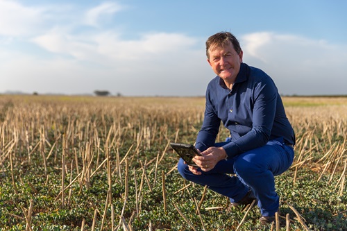 Anthony Willmott crouched in a paddock using the Rural Intelligence Platform on a tablet. 