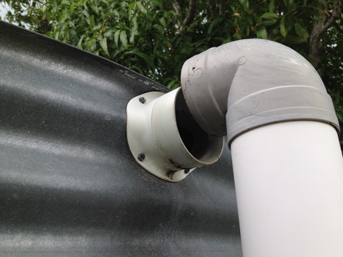 Side of a rainwater tank with a disconnected outflow pipe.