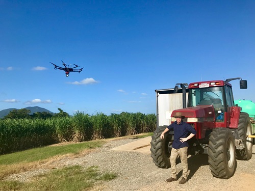 Man stands beside a tractor with a drone in the air