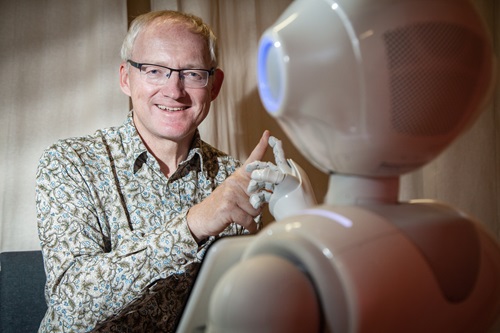 Toby Walsh touching finger-tip to finger-tip with a robot.