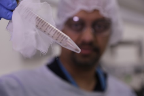 Scientist wearing protective clothing holding up a tube containing a scientific sample. 