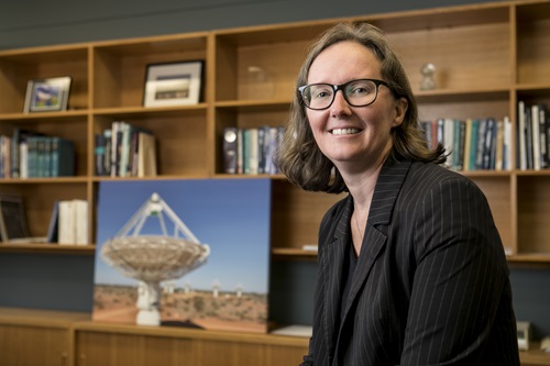 Dr Sarah Pearce sitting in an office with a picture of a telescope in the background. 