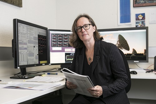 Dr Sarah Pearce sitting at a desk holding a booklet with computer monitors in the background.