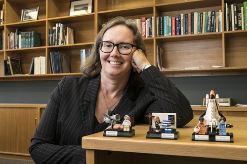 Sarah Pearce leaning on a desk in front of astronomy themed mini Lego sets.