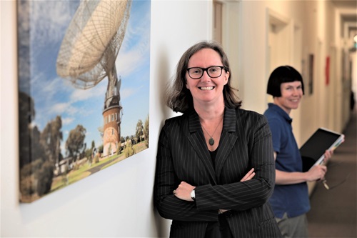 Dr Sarah Pearce leaning against a wall next to an image of a telescope. 