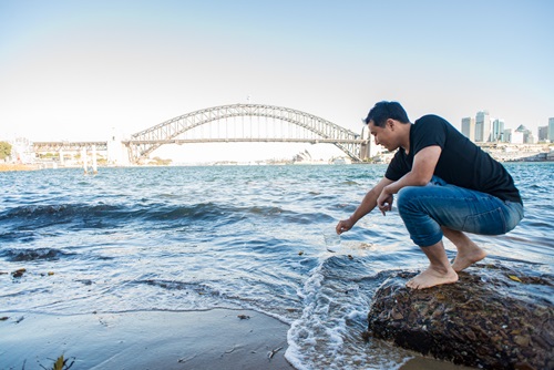 Scientist scoops water out of Sydney Harbour, with the Harbour Bridge in the background.