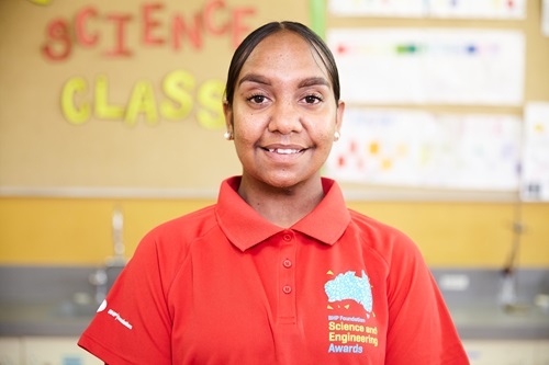 Nyheemah Cox wearing a red shirt with the BHP Foundation Science and Engineering Awards logo,and standing in a classroom.