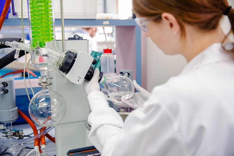 Scientist wearing protective lab coat and glasses working at a bench in a laboratory.  