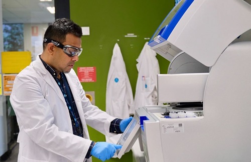 Scientist in lab coat and wearing safety glasses and gloves, working with laboratory machinery. 
