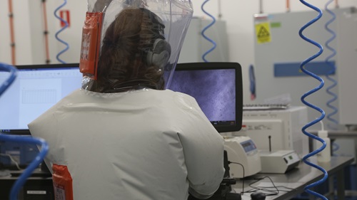 Scientist working in a laboratory at a computer screen wearing a protective suit. 