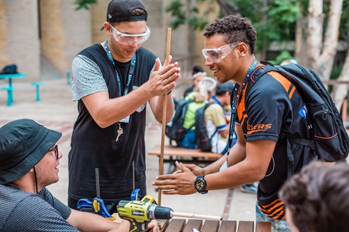 People wearing safety glasses and working on an experiment trying to start a fire by rubbing sticks.