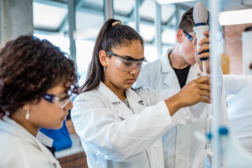 Three people in lab coats working on laboratory equipment. 