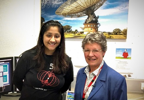 Two women standing together in an office with a picture of a telescope in the background