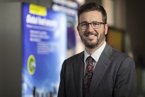 Portrait photo of Mark Stickells standing in front of blurred poster. 