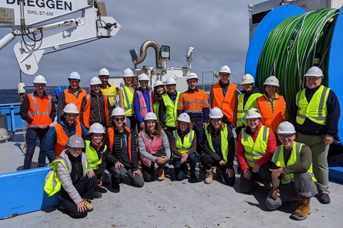 People wearng hi-vis jackets and hard hats gathered for a group photo on board the deck of RV Investigator. 