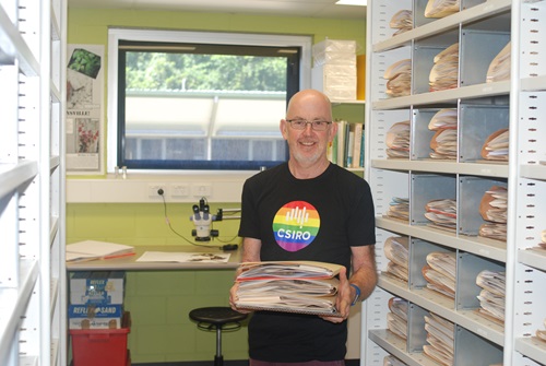 Scientist in Pride t-shirt with microscope and plant sample