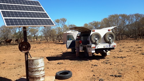Person standing next to a 4WD vehicle parked near a solar powered monitoring station in bushland.