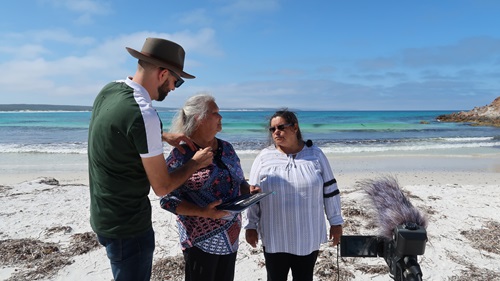 Three people standing on a beach talking with their backs to the water.