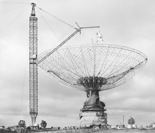 Black and whte photgraph of the Parkes telescope under partial constructions with crane tower next to the frame of the dish section.