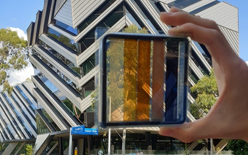A hand holds a solar cell in front of a building.