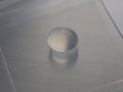 One droplet of liquid forming a circular mound is in the middle of a rectangular piece of clear vinyl.