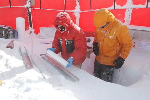 Two people in extreme weather outfits looking at an ice core. 