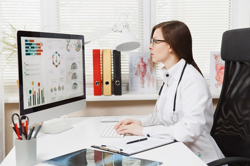 Clinician in a white coat sitting at a desk using the medtech platform on a computer.